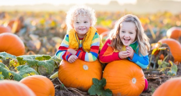 2 kids sitting on pumpkins